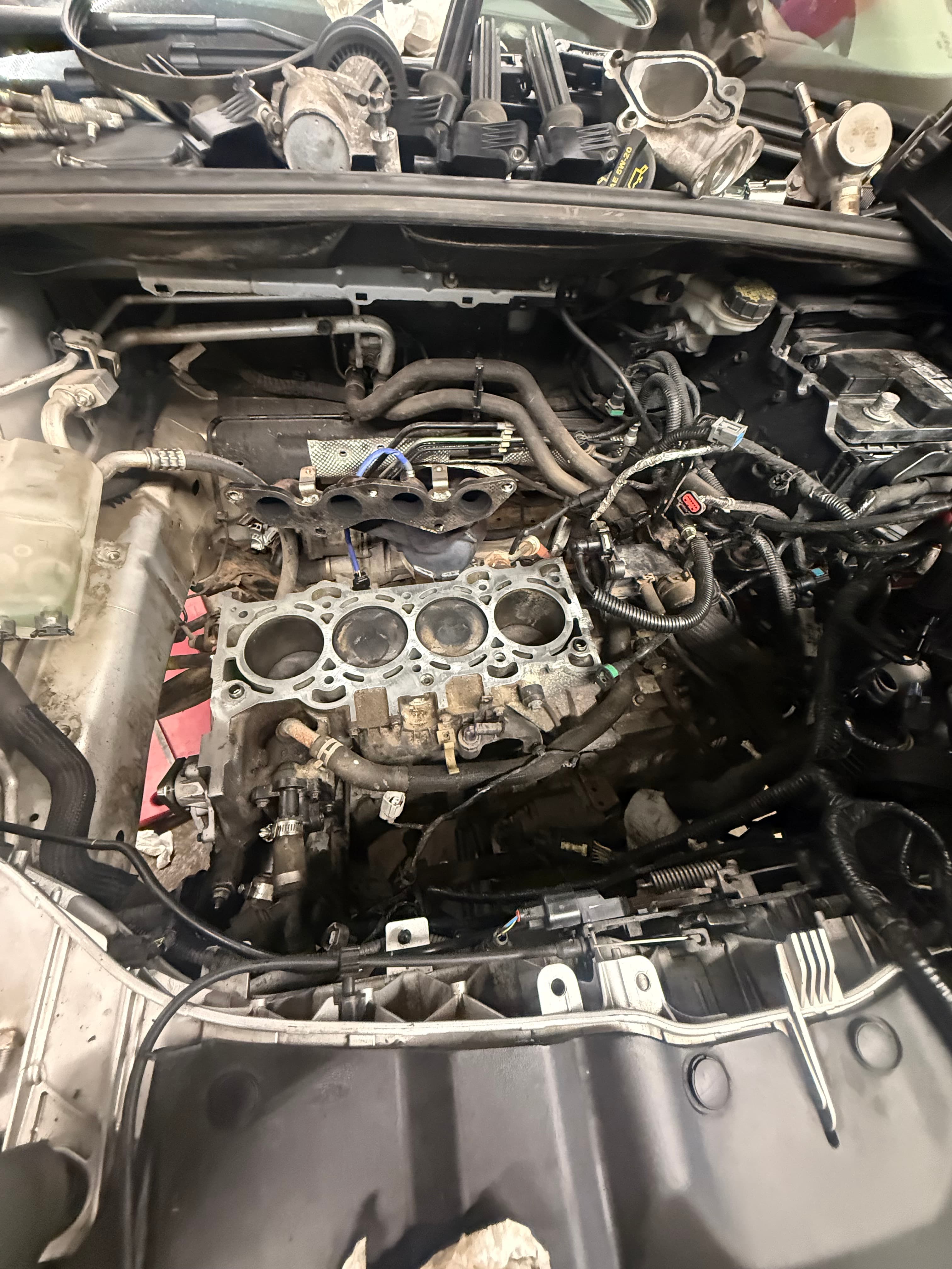 Disassembled car engine showing the cylinder block with four exposed pistons and various mechanical components.